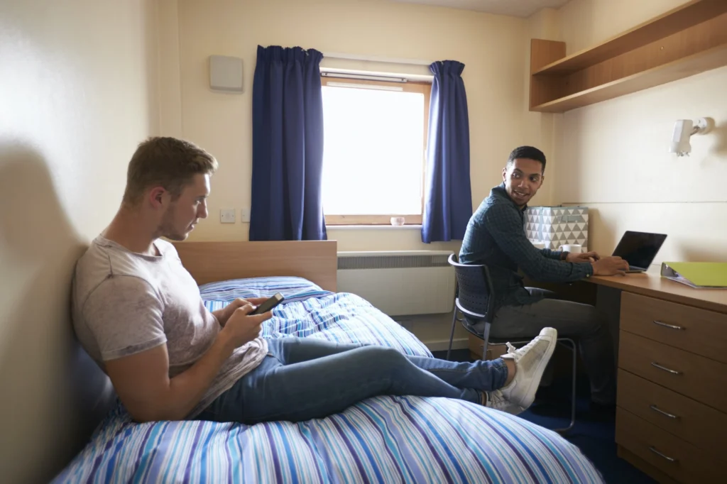 male students working in bedroom of campus accommodation